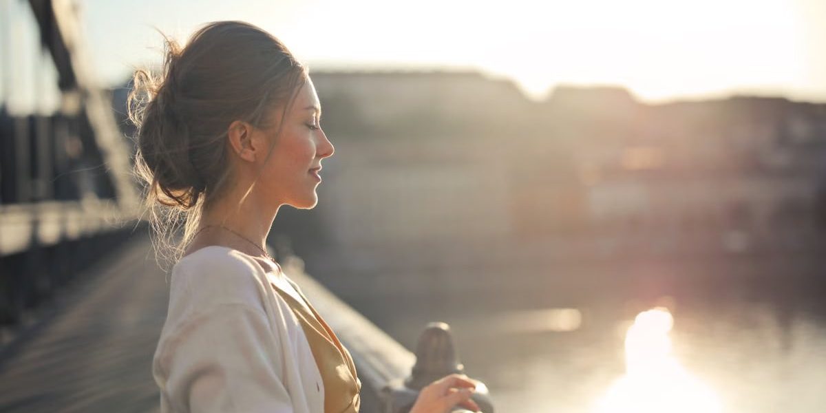 A young woman stands on a bridge enjoying the warm sunset over the city skyline.