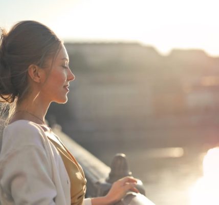 A young woman stands on a bridge enjoying the warm sunset over the city skyline.